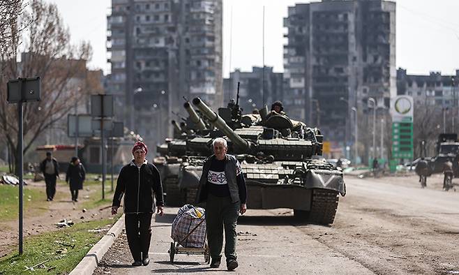 지난 15일(현지시간) 우크라이나 도네츠크 지역 마리우폴에서&nbsp;지역 주민들이 러시아의 T-80BV 탱크를 뒤에 두고 거리를 걷고 있다. TASS연합뉴스