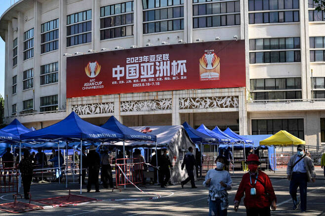 베이징에서 2023 아시안컵을 홍보하는 광고판 앞에서 사람들이 코로나19 테스트를 받고 있다. 중국은 코로나19로 인해 2023 아시안컵을 개최하지 않기로 했다.(사진=AFPBBNews)