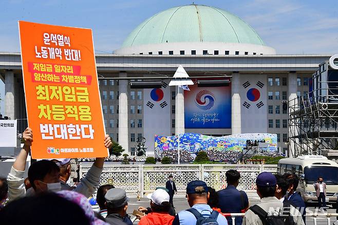 [서울=뉴시스] 전진환 기자 = 지난 10일 국회에서 제20대 대통령 취임식이 열린 가운데 국회 앞 도로에서 한 아르바이트 노조원이 '최저임금 차등적용 반대' 피켓을 들어보이고 있다. (공동취재사진) 2022.05.10.  photo@newsis.com