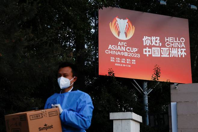 지난 14일 중국 베이징에서 방호복을 입은 남성이 AFC 아시안컵 광고판 앞을 지나가고 있다. 베이징 | 로이터연합뉴스