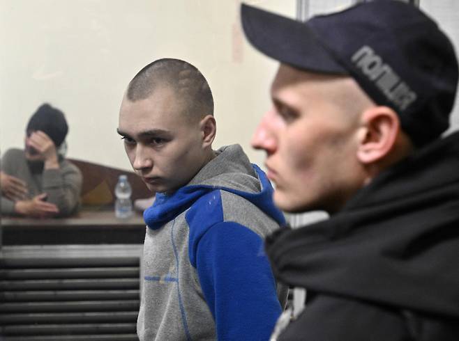 18일(현지 시각) 우크라이나 키이우 지방법원에서 러시아 육군 탱크 사단 소속 바딤 쉬시마린(21·가운데) 하사가 지난 2월 수미 지역에서 60대 민간인을 사살한 혐의로 전범 재판을 받고 있다. 그는 지난 13일 열린 심리에서 당시 범행에 대해 “사격 명령을 받고 수행한 것”이라며 혐의를 시인했다. 우크라이나 검찰은 “쉬시마린 하사가 최대 종신형에 처해질 수 있다”고 전했다./AFP 연합뉴스