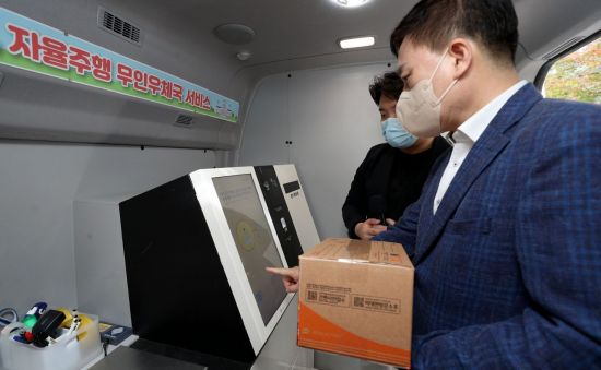 손승현 우정사업본부장이 19일 서울대에서 열린 자율주행무인우체국차량 안에서 소포우편물을 접수하고 있다.