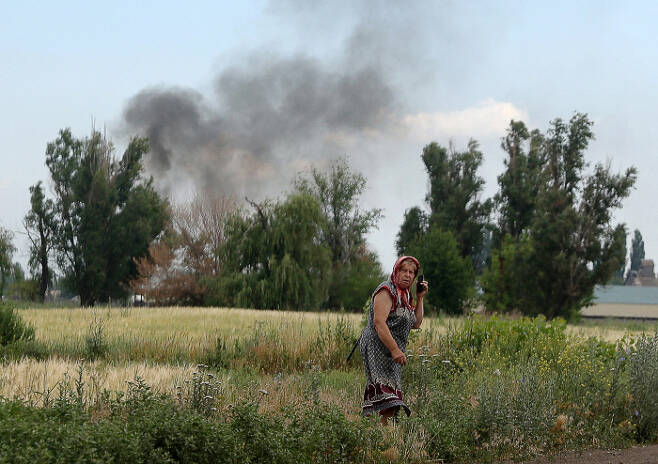 지난 23일(현지시간) 우크라이나 동부 도네츠크주의 스비아토-포크로우스케 마을 뒤편으로 연기가 치솟고 있는 가운데 한 지역 주민이 길가에서 휴대전화로 통화하고 있다. 도네츠크 | AFP연합뉴스
