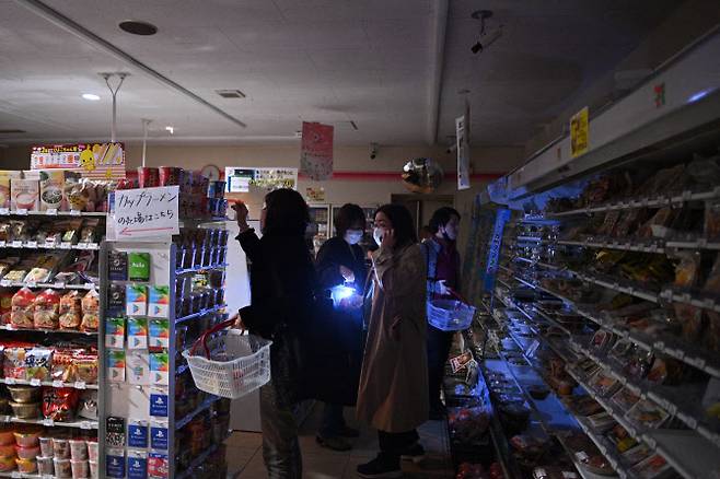 지난 3월 16일 일본 동부를 강타한 규모 7.3의 지진으로 도쿄에서 정전이 발생, 사람들이 불이 꺼진 상점에서 쇼핑하고 있는 모습.(사진=AFP)