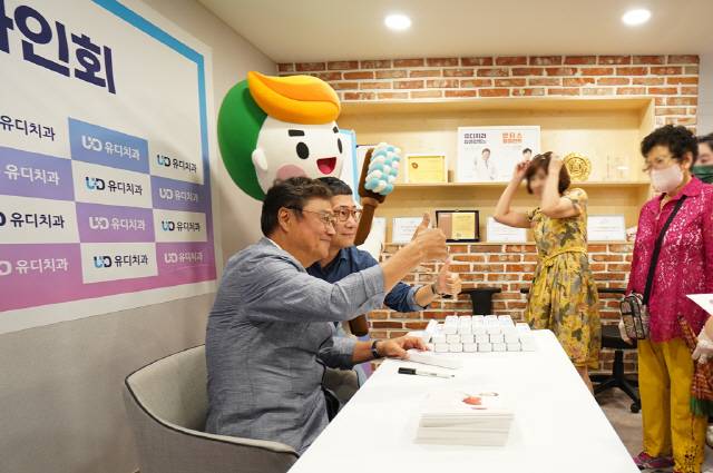 가수 남진(왼쪽)이 유디상무치과의원에서 팬사인회를 진행하고 있는 모습.
