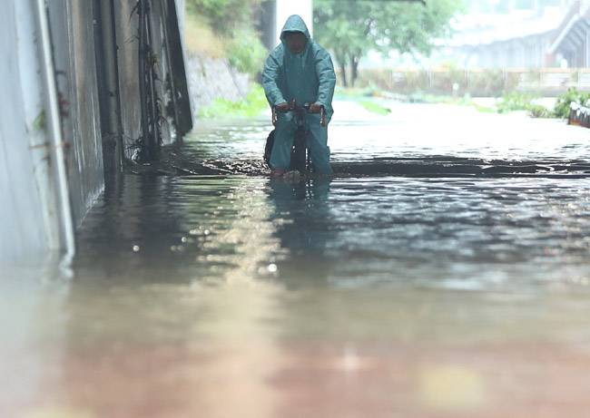 30일 오전 침수된 서울 은평구 불광천에서 시민이 물에 반쯤 잠긴 자전거를 타고 이동하고 있다. 뉴시스