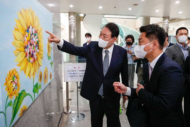 윤석열 대통령이 25일 오전 용산 대통령실에서 출근길 약식 기자회견(도어스테핑)을 마친 뒤 강선아 작가의 '해바라기II' 그림을 둘러보고 있다. 이날 대통령실 1층 양옆 벽면에는 발달장애 작가들의 작품 15점이 처음 전시됐다. /뉴스1