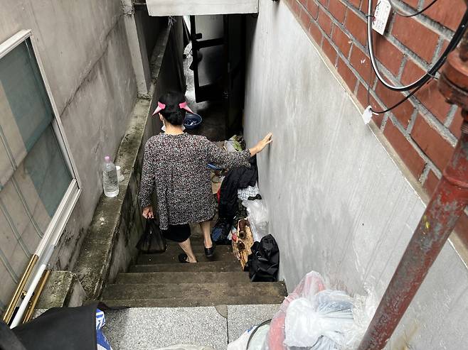 Sohn goes down the stairs leading to the entrance of her basement home. Piled up against the wall are wet household goods damaged by the rain. (Kim Arin/The Korea Herald)