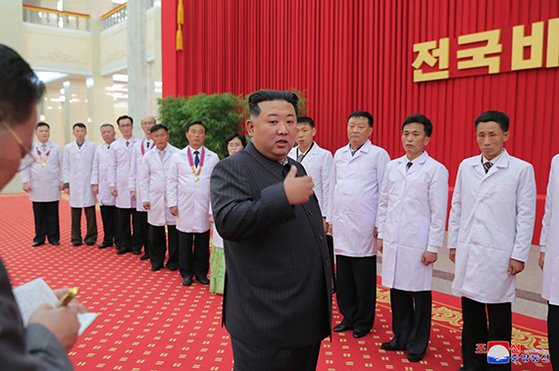김정은 북한 국무위원장이 지난 10일 전국비상방역총화회의에서 코로나19 사태 종식을 선언한 뒤 방역 및 보건부문의 일꾼들과 과학자들을 격려하고 있다. [뉴시스]