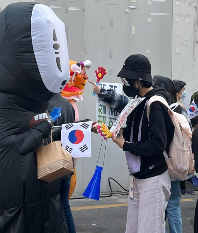 영화 '센과 치히로의 행방불명'에 등장하는 '가오나시' 에어 슈트를 입은 참가자와 스티커를 준비해온 시민이 4월 8일 서울 여의도 더불어민주당 당사 앞에서 열린 8차 개혁문화제에서 간식을 나누고 있다. 소진영 인턴기자