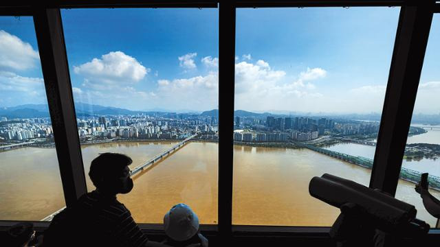 기록적인 폭우가 멈추고 모처럼 파란 하늘을 드러낸 12일 서울 여의도 63빌딩 내 '63아트'를 찾은 시민들이 맑은 하늘 아래 흐르는 누렇게 변한 한강을 바라보고 있다. 기상청은 주말인 14일 전국에 걸쳐 비가 시작돼 다음 주 초 또다시 정체전선으로 인한 폭우가 내릴 것으로 예보했다. 연합뉴스