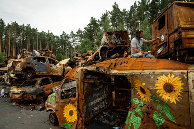 미국 예술가 트렉 선더 켈리가 12일 우크라이나 키이우 외곽 이르핀에서 러시아의 공격으로 파괴된 자동차에 우크라이나 국화인 해바라기를 그리고 있다. 이르핀=AP 뉴시스
