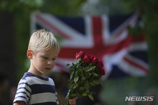 [런던=AP/뉴시스] 11일(현지시간) 영국 런던의 버킹엄 궁전 옆에 있는 그린 파크 추모소에서 한 소년이 꽃을 들고 엘리자베스 2세 여왕을 추모하고 있다. 2022.09.12.