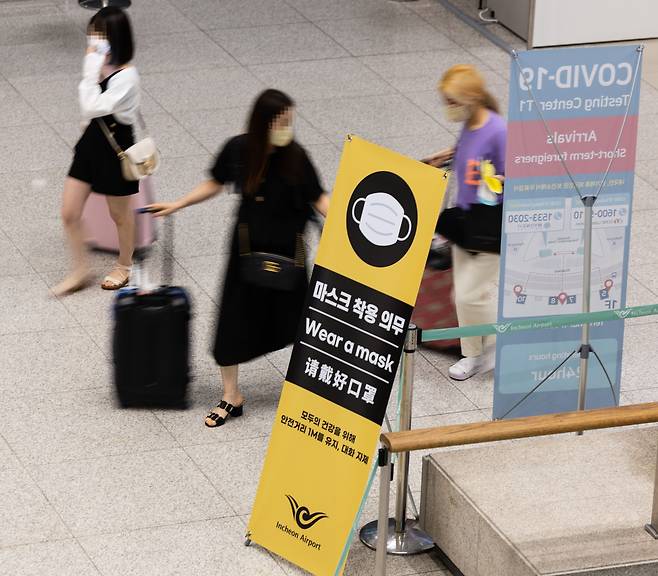 지난 4일 오후 인천공항을 통해 입국한 여행객들이 마스크 착용과 입국 뒤 코로나19 검사소 위치 안내가 담긴 홍보물 앞을 지나가고 있다. /연합뉴스