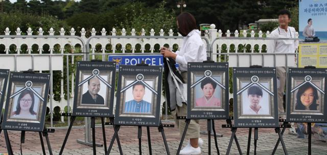 코로나19 백신 피해자 가족이 지난 15일 서울 여의도 국회 앞에 놓인 코로나19 백신 사망자들의 영정 뒤로 지나가고 있다. 뉴스1