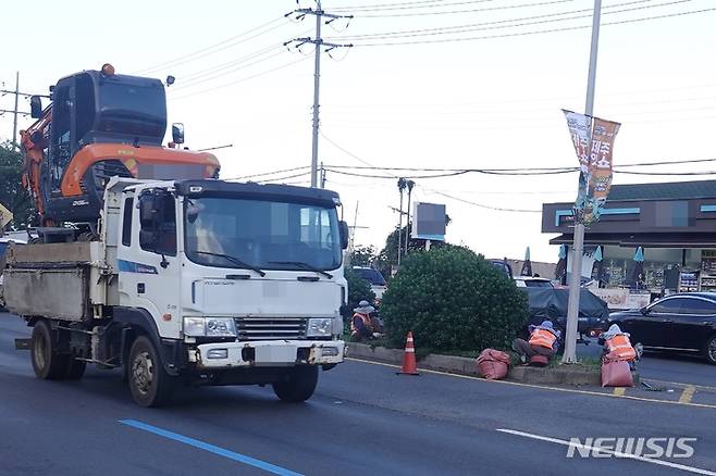 [제주=뉴시스] 22일 오전 제주시 노형동 도로 경계석 화단에서 3~4명의 인부들이 위험하게 잡초 제거 작업을 하고 있다. 바로 옆 차선에는 굴삭기를 실은 트럭이 달리고 있다. 2022.09.22. oyj4343@newsis.com