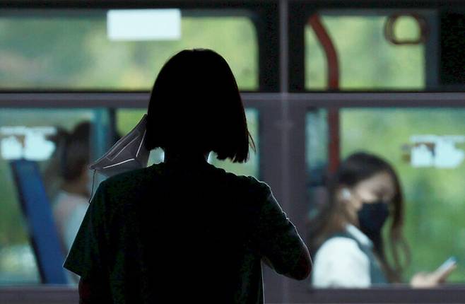 지난 20일 서울 서대문구 대학가에서 한 학생이 마스크를 벗은 채 횡단보도 신호를 기다리고 있다. 지나가는 버스 안 마스크 착용 승객과 대조를 이룬다. 연합뉴스