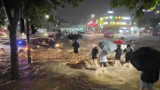 중부지방을 중심으로 폭우가 쏟아진 지난달 8일 밤 서울 관악구 도림천이 범람, 시민들이 아슬아슬하게 물살을 헤쳐 길을 건너고 있다. 뉴스1