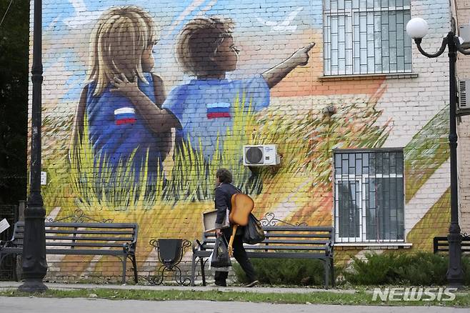 [루한스크=AP/뉴시스] 27일(현지시간) 우크라이나 동부 루한스크인민공화국(LPR) 루한스크에서 한 남성이 러시아 국기가 그려진 옷을 입은 어린이들 벽화를 지나고 있다. 우크라이나 내 러시아 점령지의 러시아 영토 편입을 위한 주민투표가 마무리돼 압도적 찬성률로 가결됐다. 이에 따라 러시아는 이들 지역에 대한 영토 편입 절차를 신속히 진행할 것으로 보인다. 2022.09.28.