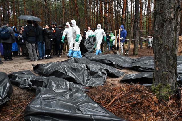 지난달 23일 우크라이나 동부 이지움의 한 숲에서 우크라이나 수사관들이 러시아군에 학살당한 뒤 매장된 시신들을 수습하고 있다. 이지움=AFP 연합뉴스
