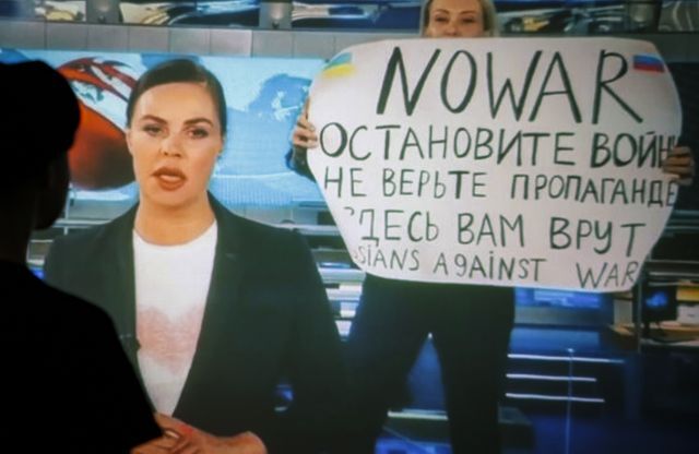 러시아 채널1 편집자 마리아 오브샤니코바(사진 속 화면 오른쪽)는 지난 3월 14일(현지시간) 저녁 자사 생방송 도중 뉴스를 전하는 앵커 뒤에 반전 팻말을 들고 나타났다. 그 장면을 러시아 수도 모스크바의 한 시민이 바라보고 있다. EPA연합뉴스