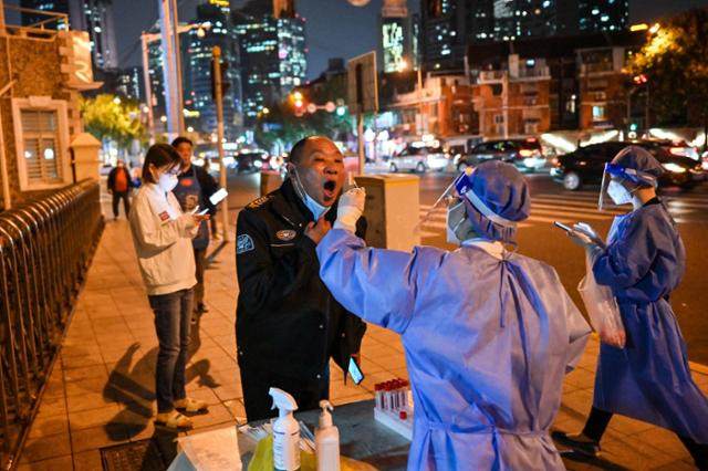 지난 1일 중국 상하이의 거리에서 한 노동자가 코로나19 PCR 검사를 받고 있다. 상하이=AFP 연합뉴스