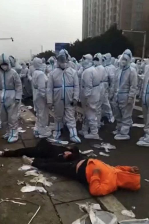중국 폭스콘 공장 시위 현장에서 방역복을 입은 경찰로 추정되는 이들이 쓰러진 노동자를 바라보고 있다./트위터 캡처