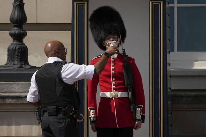 지난 7월 18일(현지시간) 폭염이 닥친 영국 런던의 버킹엄궁 밖에서 한 경찰관이 곰털 모자를 쓰고 근무하는 왕실 근위병에게 물을 주고 있다. 사진=AP연합뉴스