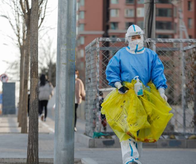 방역복 사라질까 중국 정부가 코로나19 방역지침을 완화하는 조치를 발표한 7일 베이징에서 방역복을 입은 한 자원봉사자가 의료폐기물 수거용 비닐을 가지고 바쁜 걸음을 옮기고 있다. 베이징 | EPA연합뉴스