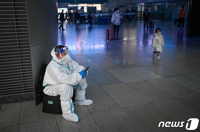 8일(현지시간) 중국 베이징 남역에서 개인보호장비(PPE)를 착용한 남성이 짐 가방 위에 앉아 휴대폰을 들여다 보고 있다. 중국은 지난 11월 말 당국의 고강도 방역 통제 '제로 코로나' 정책에 항의하는 백지시위가 일어난 이후 '위드 코로나'로 방역 기조를 전환했다. ⓒ AFP=뉴스1 ⓒ News1 권진영 기자