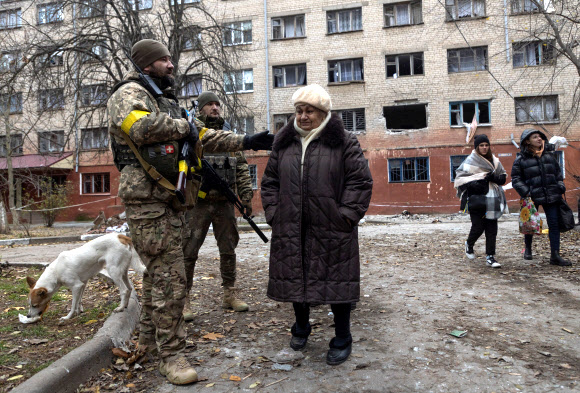 11일(현지시간) 러시아군의 공습으로 파괴된 우크라이나 동부 헤르손에 있는 건물 앞에서 우크라이나군이 한 여성과 대화하고 있다.헤르손 로이터 연합뉴스