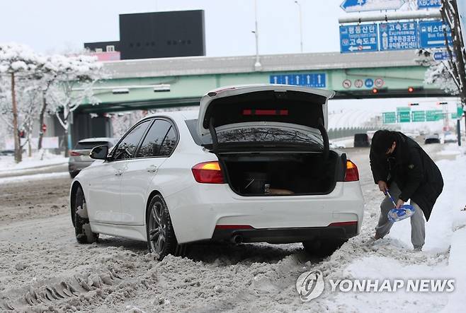 눈길 벗어나려 안간힘 (광주=연합뉴스) 천정인 기자 = 대설특보가 발령된 18일 광주 서구 한 도로에서 한 시민이 차량 아래에 쌓인 눈을 치우고 있다. 2022.12.18 iny@yna.co.kr