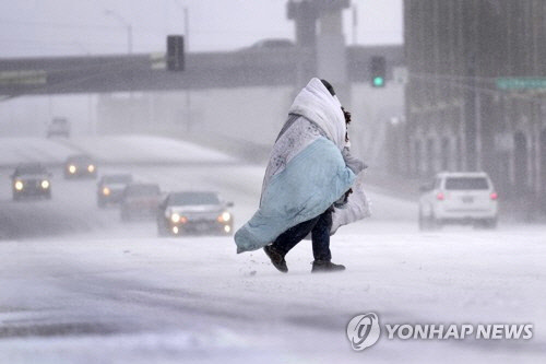 미국 세인트루이스에서 눈이 내리는 가운데 담요를 두르고 길을 건너는 한 시민. [세인트루이스 AP=연합뉴스]