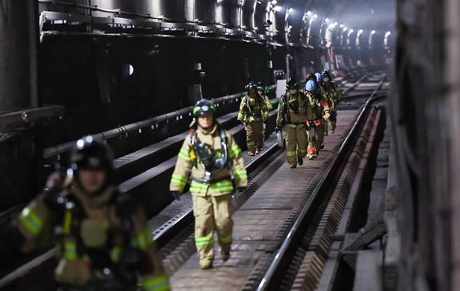 Firefighters walks along a tunnel between Muakjae Station and Dongnimmun Station on Friday. (Yonhap)