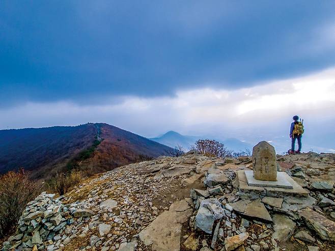 고헌산 서봉 전경. 먹구름 덮인 산 아래가 고헌산 정상이고, 등산인이 바라보는 쪽에 가지산, 능동산, 천황산 등이 솟아 있다. 미세먼지가 자욱해 산줄기만 아른거린다.