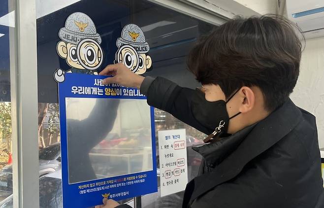 경찰이 무인점포에 양심거울을 부착하고 있다.