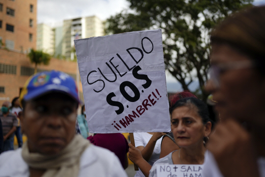 지난 19일(현지시간) 베네수엘라 카라카스의 보건부 앞에서 베네수엘라의 공공 근로자, 연금 수급자들이 ‘월급, SOS, 굶주림’이라고 쓴 팻말을 들고 시위에 나서고 있다. AP 뉴시스