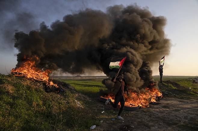 팔레스타인 주민들이 26일(현지시간) 가자지구 동쪽 이스라엘과의 국경지역에서 이스라엘의 제닌 난민촌 공격에 항의하며 타이어를 태우고 국기를 흔들고 있다. AP연합뉴스