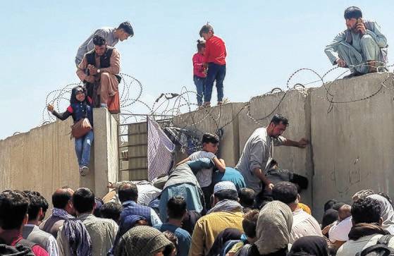 아프가니스탄 수도 카불의 하미드 카르자이 국제공항에서 국외 탈출을 위해 주민들이 담을 넘어 공항으로 들어가고 있다. [로이터=연합뉴스]