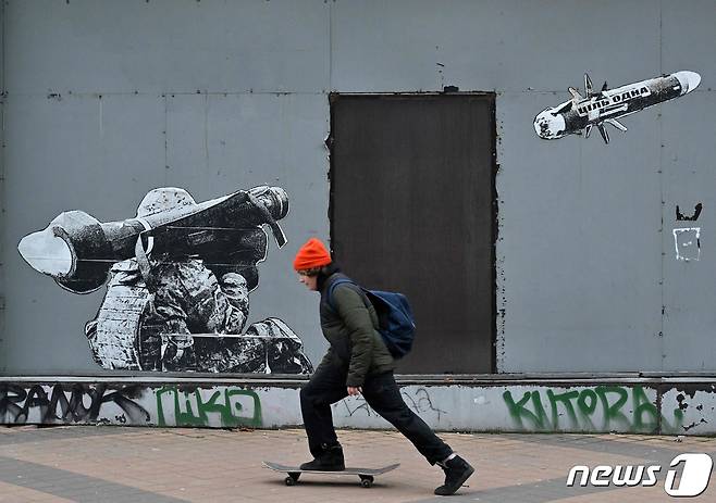 우크라이나 키이우에서 병사가 휴대용 대전차 미사일을 발사하는 모습을 그린 벽화 앞에 소년에 스케이트 보드를 타고 있다. ⓒ AFP=뉴스1