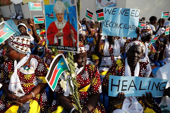2023년 2월14일 남수단 수도 주바의 성데레사 성당에서 신자들이 프란치스코 교황의 미사 집전을 기다리고 있다. “우리는 화해가 필요합니다”, “힐링(치유)”라고 쓴 손팻말이 보인다. 주바/로이터 연합뉴스