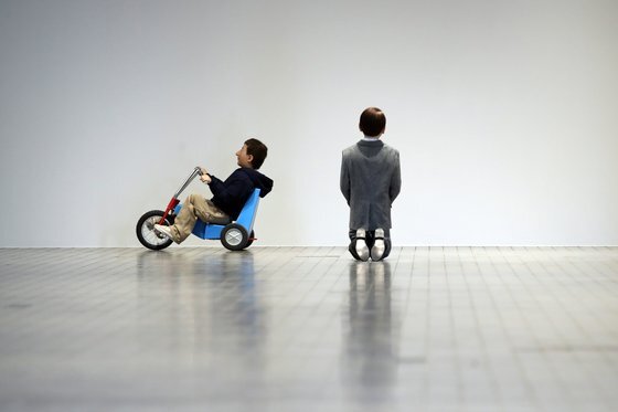 마우리치오 카텔란의 인물 작품은 실제의 60% 규모로 만들어져 보는 이에게 기이한 느낌을 전달한다. 세발자전거를 타고 전시장을 누비는 '찰리'(왼쪽)와 무릎 꿇은 히틀러의 뒷모습. [사진 뉴시스]
