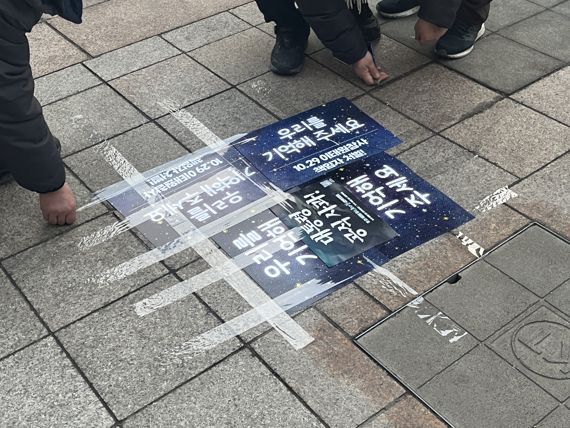 이태원 유가족 측이 바닥에 떨어진 2차 계고장 위에 포스터를 붙이고 테이프로 봉인하고 있다. /사진= 주원규 기자