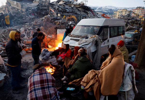지난 8일 튀르키예 카라만라스에서 지진 여파로 무너진 건물 현장 인근에서 사람들이 불 옆에 둘러앉아 있다. 로이터 연합뉴스