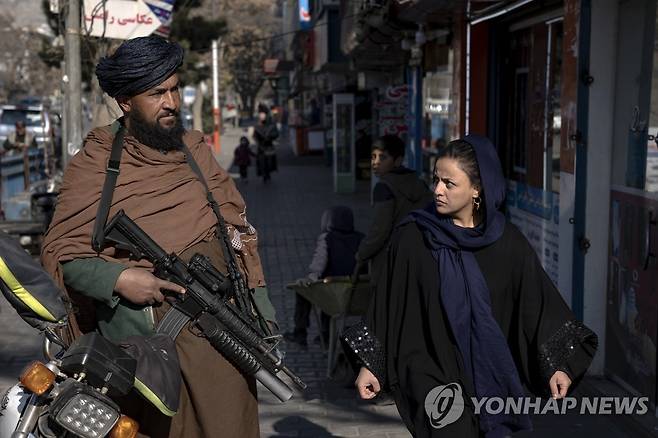 카불 시내에서 총을 들고 선 아프가니스탄 전사 곁으로 한 여성이 지나가고 있다. [AP 연합뉴스 자료사진. 재판매 및 DB 금지]