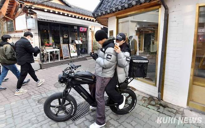 젊은이들이 오토바이를 타고 익선동 골목 내 맛집을 검색하고 있다.