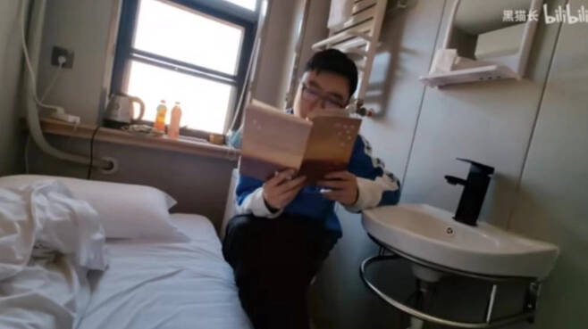 중국의 한 블로거가 허난성 정저우에 있는 초소형 호텔을 체험하고 올린 영상 사진. 변기에 앉아 책을 읽고 있는 모습이다. 현지에선 시험을 앞둔 수험생들에게 인기가 높다고 한다. [SCMP 홈페이지 갈무리]