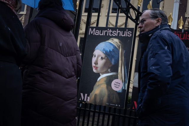 네덜란드 시민들이 9일(현지시간) 헤이그 마우리츠호이스 미술관 입구에서 요하네스 베르메르의 그림 '진주 귀걸이를 한 소녀' 광고를 지나가고 있다. AFP 연합뉴스