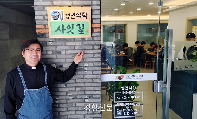 김회인 신부가 13일 전북대학교 신 정문 인근에 문을 연 청년을 위한 ‘청년식탁 사잇길’ 식당 앞에서 현판을 가리키며 취지를 설명하고 있다. 김창효 선임기자