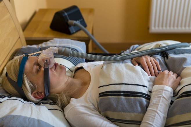 폐쇄성수면무호흡증이 심해 양압기(CPAP)를 착용하고 잠자는 여성. 콜레스테롤약 스타틴을 복용하면 이들 환자의 심장병 위험이 낮아지는 걸로 나타났다. [사진=게티이미지뱅크]